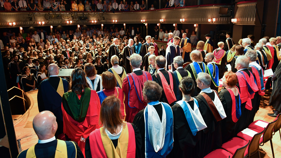 RCM staff in robes on the Britten Theatre stage during a graduation ceremony